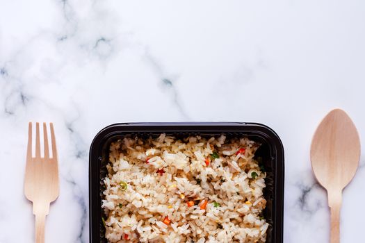 Delicious fried rice in lunch box with wooden spoon and fork on marble background for ready to eat and food concept
