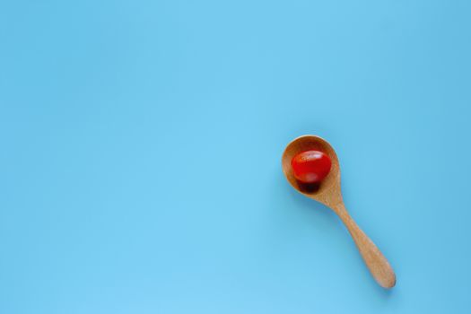 Fresh red tomato in wooden spoon on blue background for diet and heathy eating concept