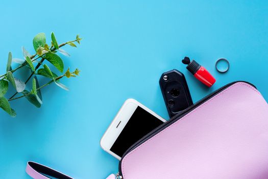 Top view of pink lady bag with smartphone, car key, red lipstick, ring and decorated flower on blue background for women accessories and lady lifestyle concept