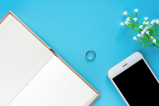 Top view of opened diary notebook with smartphone and decorated items on blue background for media technology and workspace concept