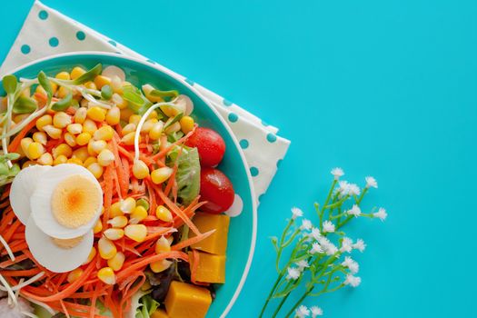 Fresh salad vegetable with boiled chicken egg and decorated flower on blue background for healthy eating and diet food concept