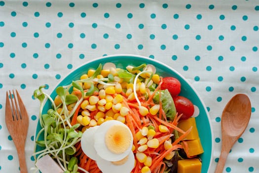 Fresh salad vegetable with boiled chicken egg, wooden spoon and fork on blue polka dot fabric or tablecloth background for healthy eating and diet food concept