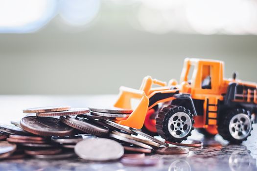 The yellow toy bulldozer with pile of coins against blurred background for saving money, investment, business and finance concept