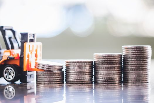 The yellow toy forklift with pile of coins against blurred background for saving money, investment, business and finance concept