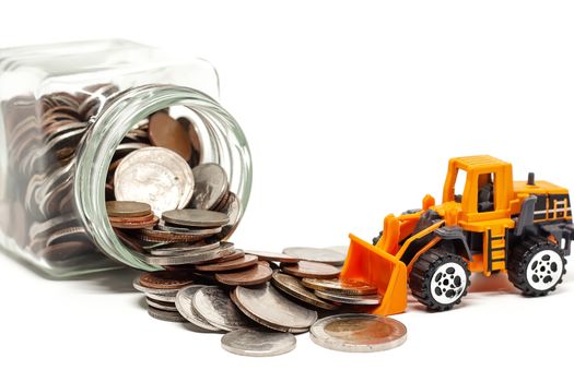 A yellow toy bulldozer with pile of coins and the glass jar on white background for saving money, investment, business and finance concept