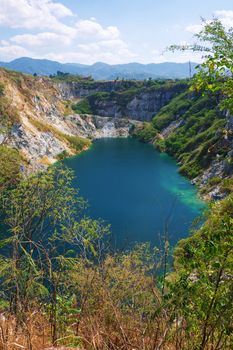 Beautiful scenic of a mining quarry with a waterlogging area in the middle against the mountain and blue sky background which is a tourist attraction in Chon Buri, Thailand