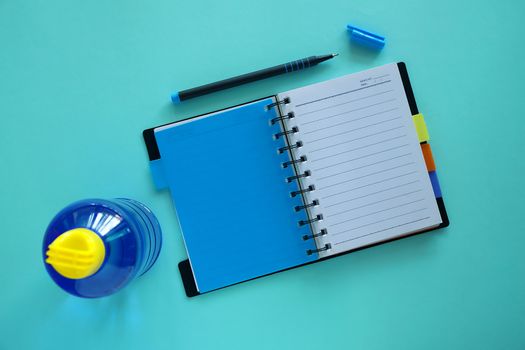 Opened notebook with pen and water bottle on blue background for healthy lifestyles concept