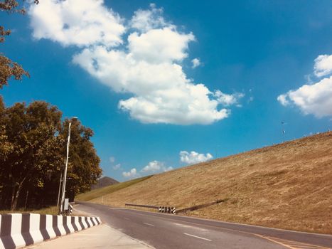 Rural country road amidst green trees with fluffy clouds and blue sky background for travelling and transportation concept