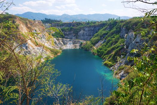 Beautiful scenic of a mining quarry with a waterlogging area in the middle against the mountain and blue sky background which is a tourist attraction in Chon Buri, Thailand