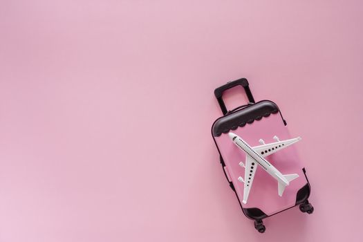 White airplane model with pinky luggage on pink background for travel and journey concept