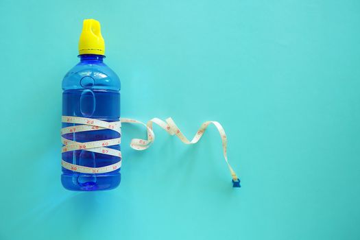 Drinking water bottle with measure tape on blue background for healthy care concept