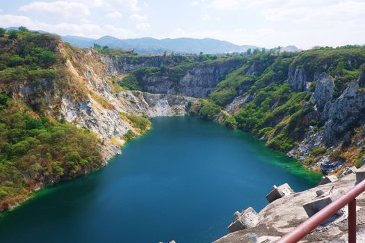 Beautiful scenic of a mining quarry with a waterlogging area in the middle against the mountain and blue sky background which is a tourist attraction in Chon Buri, Thailand