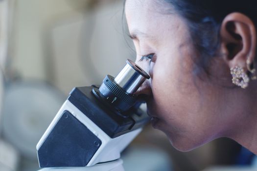 Close up of woman using a microscope in a laboratory - Female scientist busy in looking into microscope