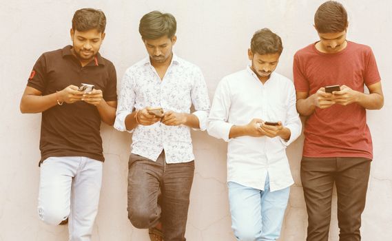 Young people with heads down busy on smart phone - Friends group using smartphone againt wall at backyard - Concept of millennials addicted and connected always to technology.
