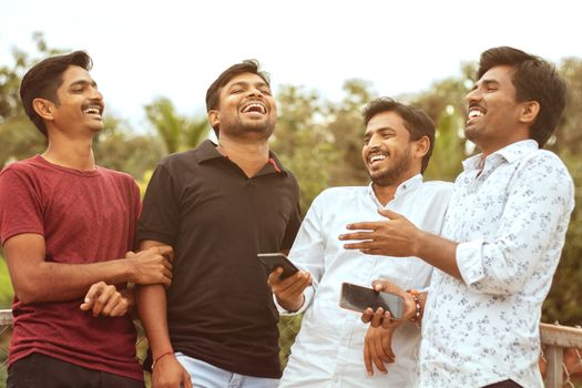 Multi racial friends having fun outdoor laughing by watching into the mobile - concept of diversity and friendship