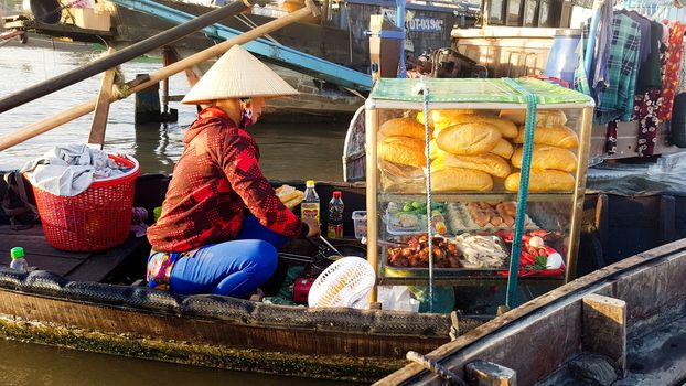 A street food vendor selling banh mi in a wooden boat at the famous Cai Rang Floating Market in Can tho, Vietnam