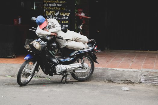 Editorial. A motorbike driver sleeps on his moto while waiting for passenger in Phnom Phen Cambodia