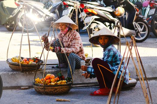 Editorial. Vietnamese street vendors selling fruits using a carrying pole in the ancient town of Hoi an, Vietnam