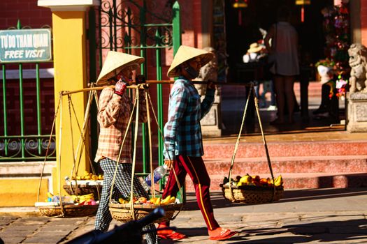 Editorial. Vietnamese street vendors selling fruits using a carrying pole in the ancient town of Hoi an, Vietnam