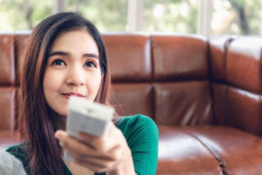 Close-Up of Asian Woman is Turn-On/OFF Air Conditioner Split Type by Remote Controller in Living Room. Electronic Air Conditioning for Comfortable Temperature in Living Room, Electric Cooling System.