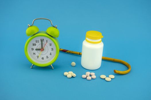 Old-age medication and healthcare concept with pharmaceutical bottle and tablets, a walking stick ant green alarm clock over a colorful blue background
