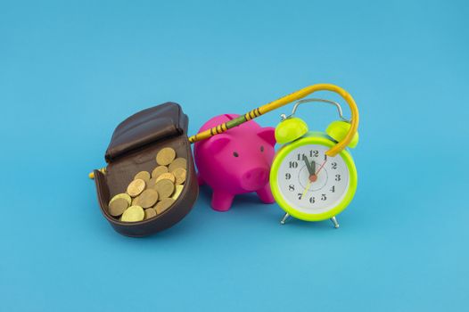 Saving for old-age and retirement concept with open purse with coins, walking stick, alarm clock and piggy bank over a blue background with copy space