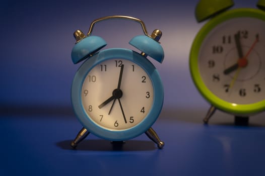 Blue and yellow twin bell analog alarm clocks over a glowing blue background with copy space