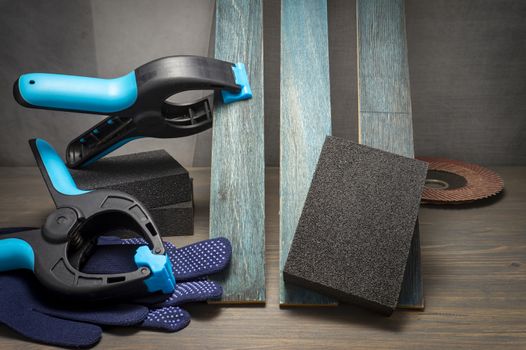 DIY renovation concept still life with safety gloves and small clamps attached to a plank of upright wood in close up