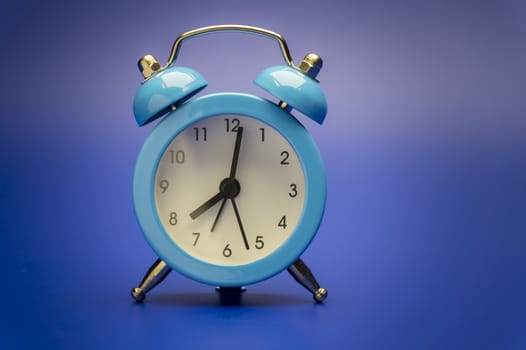 Blue twin bell analog alarm clock over a colorful blue background with copy space