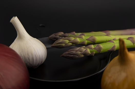 Skillet with fresh raw green spring asparagus spears and assorted red and white onions with garlic bulb ready for cooking