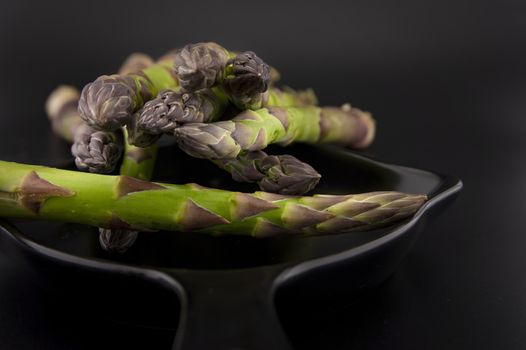 Skillet with fresh raw green spring asparagus spears ready for cooking over a black background with copy space