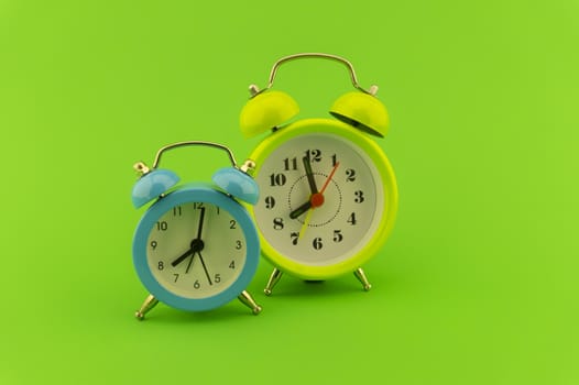 Blue and yellow twin bell analog alarm clocks over a colorful green background with copy space
