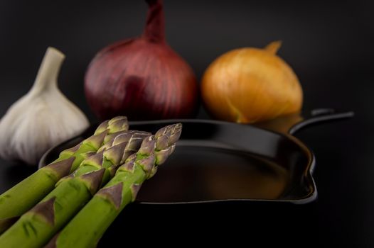 Skillet with fresh raw green spring asparagus spears and assorted red and white onions with garlic bulb ready for cooking