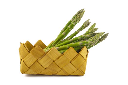 Bundle of fresh green asparagus in a rustic woven basket isolated on white background, selective focus in a low angle view