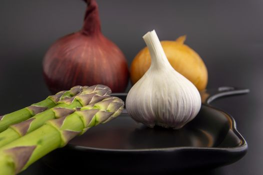 Skillet with fresh raw green spring asparagus spears and assorted red and white onions with garlic bulb ready for cooking