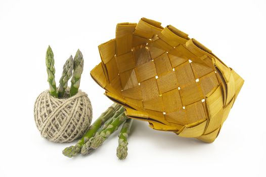 Bundle of fresh green asparagus, rustic woven basket and ball of natural hemp twine isolated on white background, selective focus in a low angle view