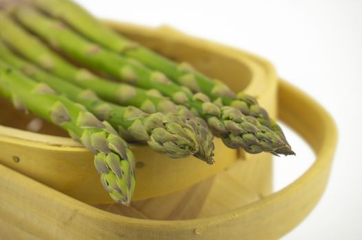 Bundle of fresh green asparagus in a rustic woven basket isolated on white background, selective focus