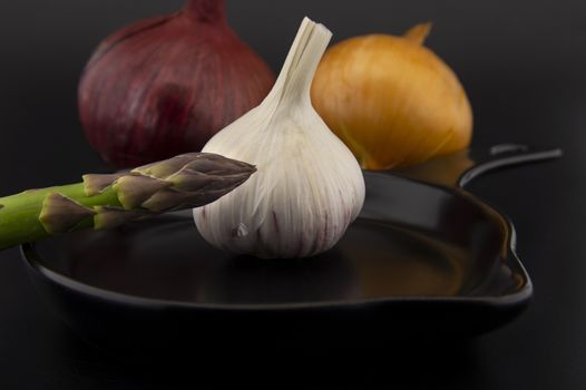 Skillet with fresh raw green spring asparagus spears and assorted red and white onions with garlic bulb ready for cooking