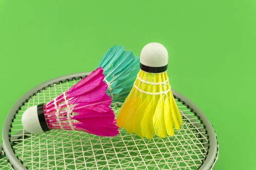 Badminton rackets and colorful feathered shuttlecocks in blue, yellow and pink on green background in a close up view