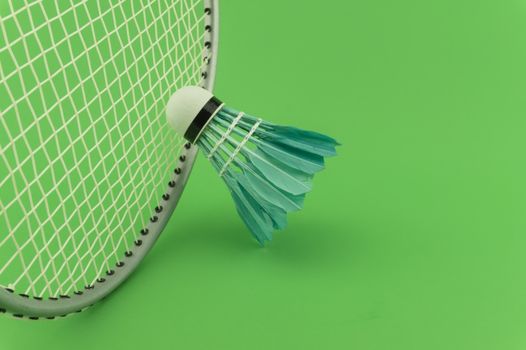 Badminton rackets and blue feathered shuttlecocks on green background in a close up view