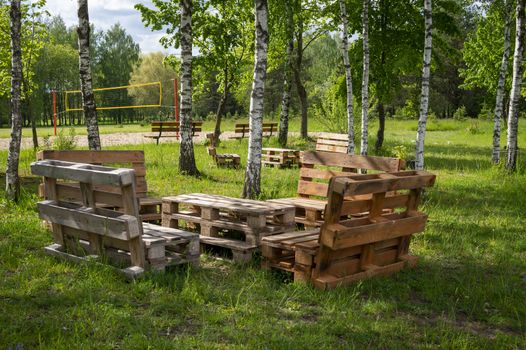 Rustic wooden table and benches made with pallets on the shore of a tranquil a lake surrounded by trees and greenery in summer sunshine