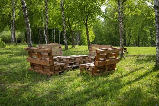 Rustic wooden table and benches made with pallets on the shore of a tranquil a lake surrounded by trees and greenery in summer sunshine