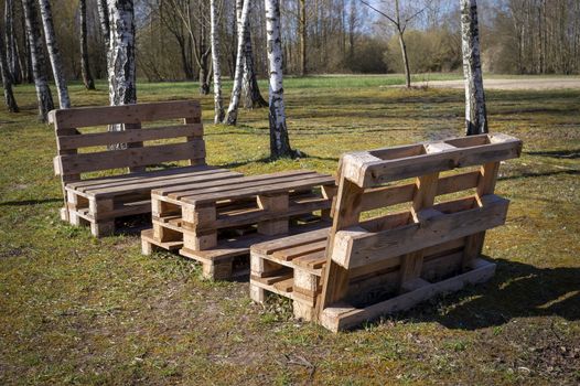 Rustic wooden table and benches made with pallets on the shore of a tranquil a lake surrounded by trees and greenery in summer sunshine