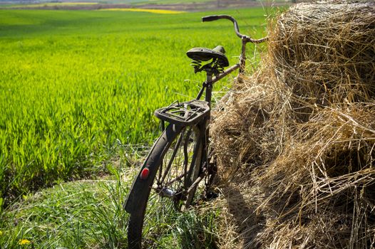 Rusty old bicycle parked against freshly harvested hay in a lush green farm field in spring in an agricultural landscape