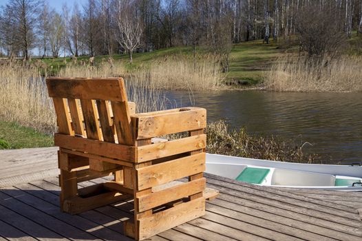 Rustic hand crafted chair made from wood pallets on wooden deck overlooking a river or lake with reeds in spring sunshine