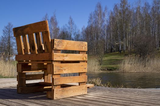 Rustic hand crafted chair made from wood pallets on wooden deck overlooking a river or lake with reeds in spring sunshine