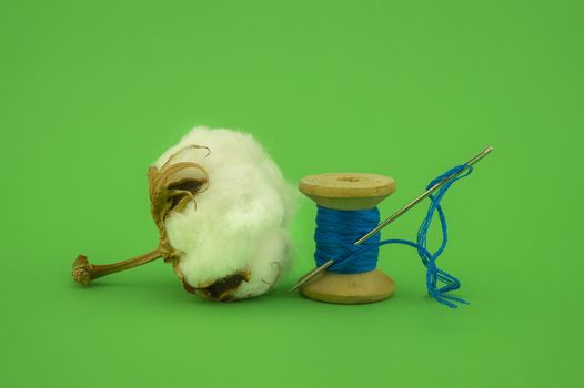Cotton boll with natural cotton and reel of bright yarn over a green background with copy space, concept of production of natural resources