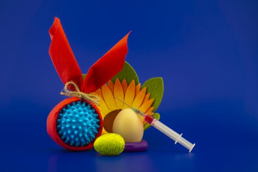 Close-up of Easter arrangement with eggs, flower, syringe and a Coronavirus or Covid-19 symbol on blue background for copy space