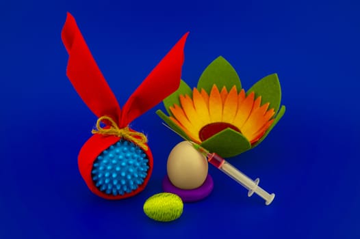Close-up of Easter arrangement with eggs, flower, syringe and a Coronavirus or Covid-19 symbol on blue background for copy space