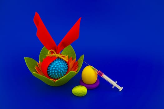 Close-up of Easter arrangement with eggs, flower, syringe and a Coronavirus or Covid-19 symbol on blue background for copy space